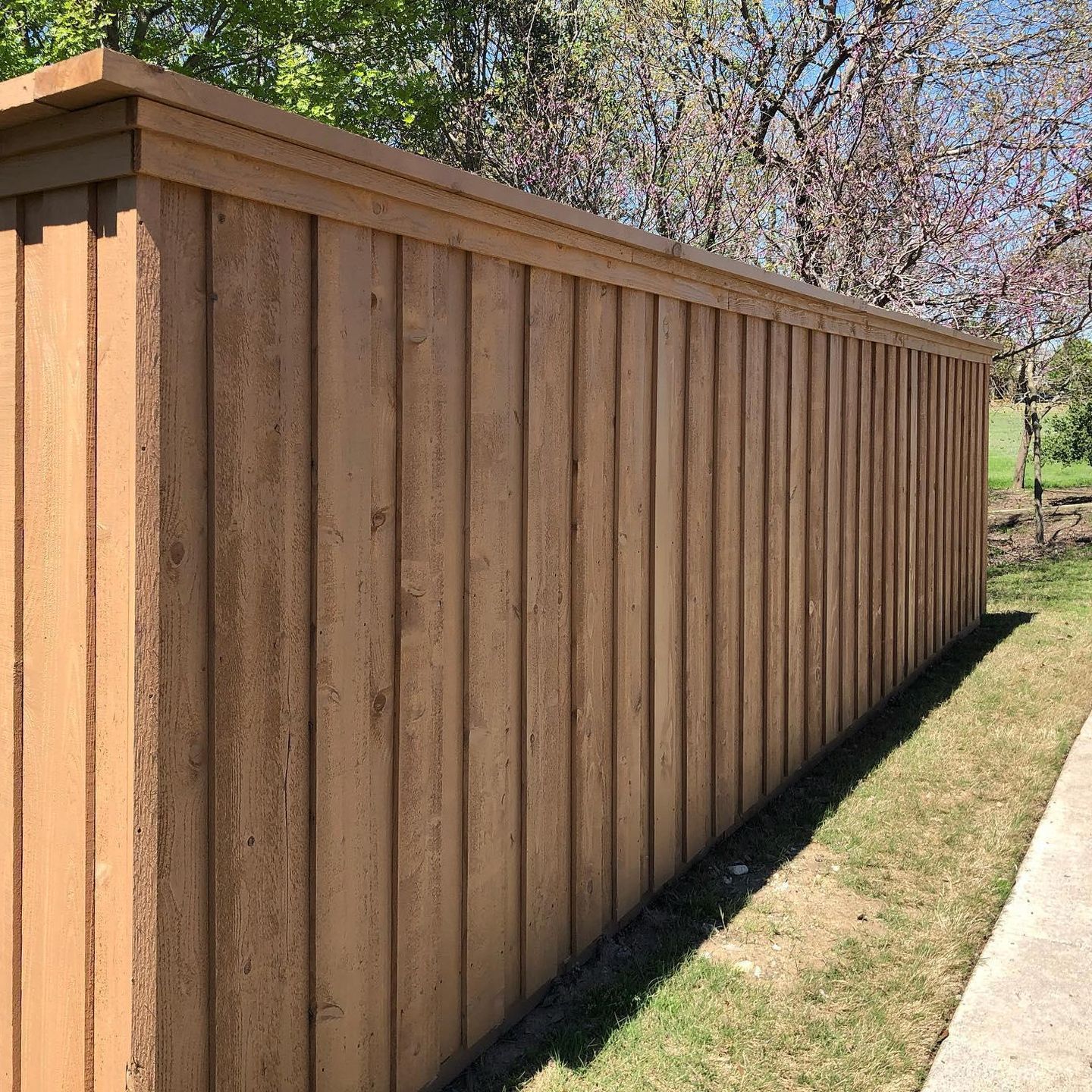 A wooden fence is sitting next to a sidewalk.