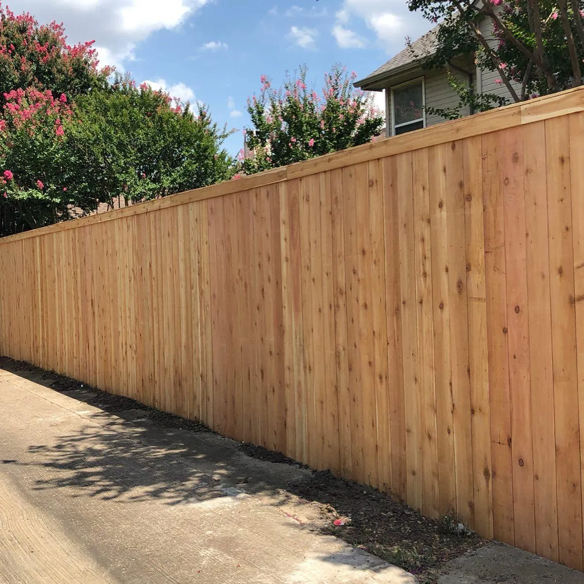 A wooden fence is sitting on the side of a road next to a house.