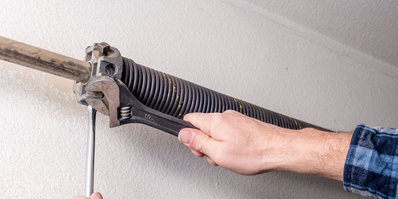 A man is fixing a garage door spring with a wrench.