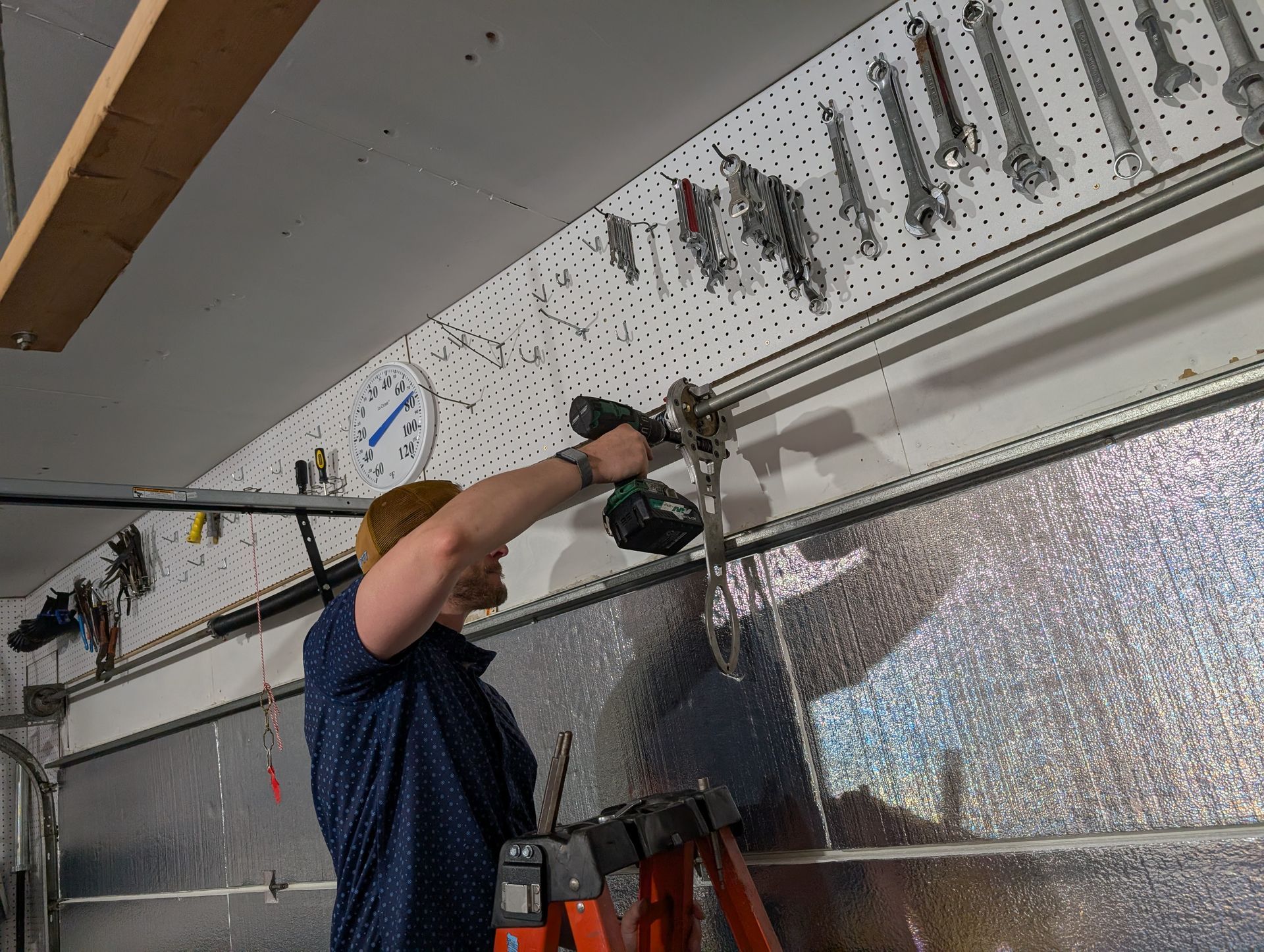 Worker drilling into a wall-mounted rail above a large insulated panel in an industrial garage