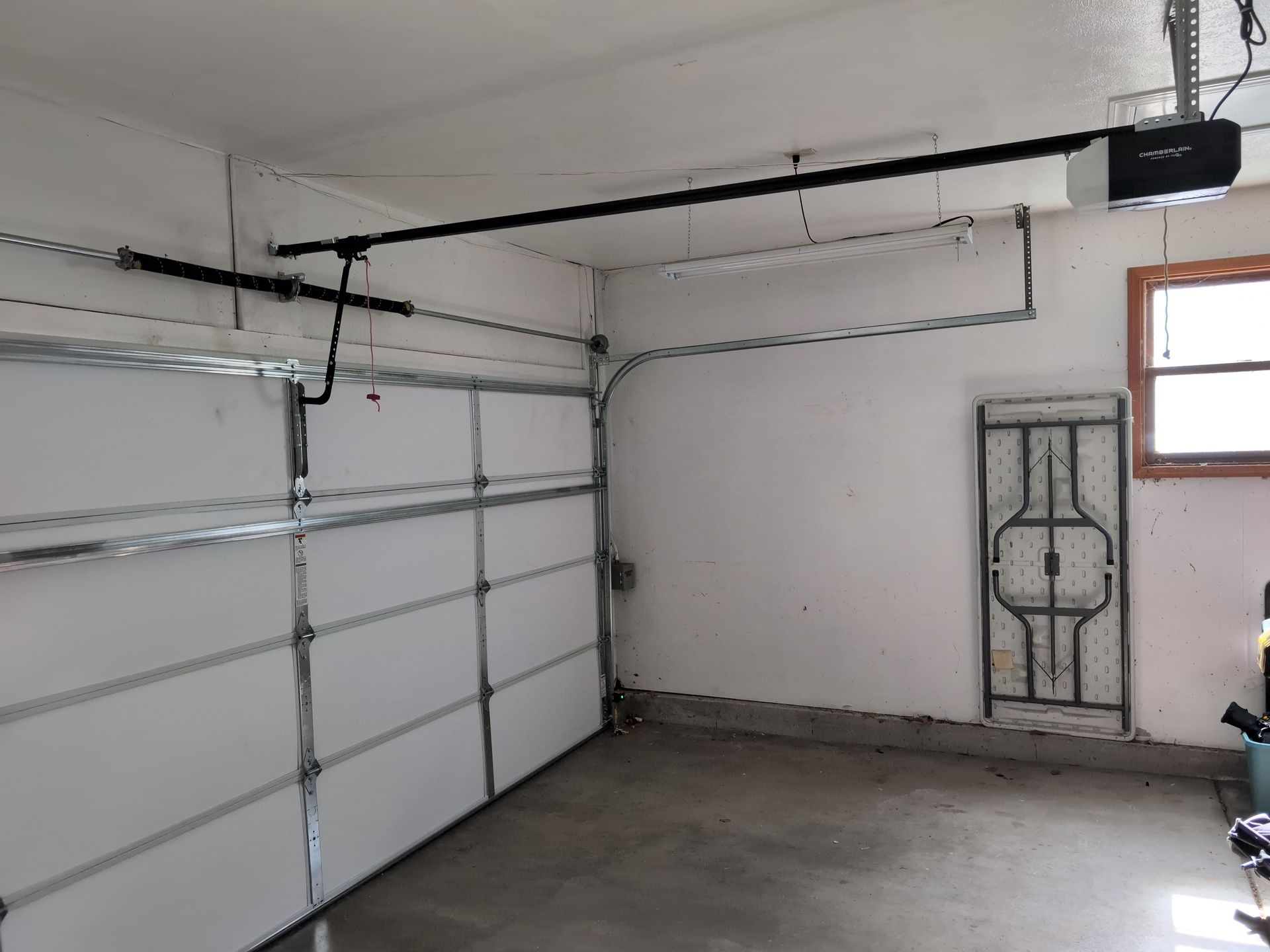 Empty garage with closed white sectional door, concrete floor, and a side entry door with window.