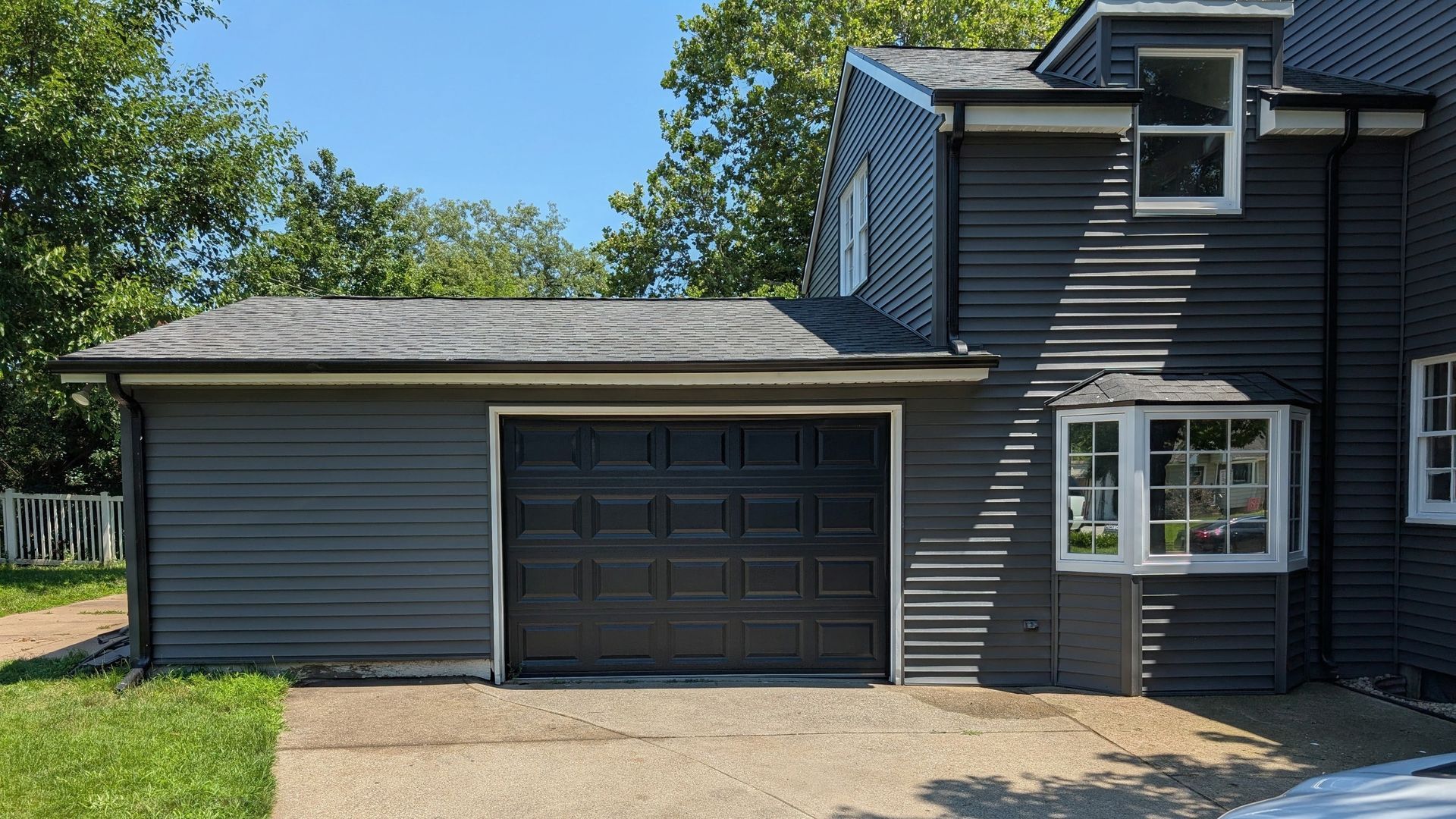 Gray house exterior with attached garage, dark trim, and a small window under a blue sky