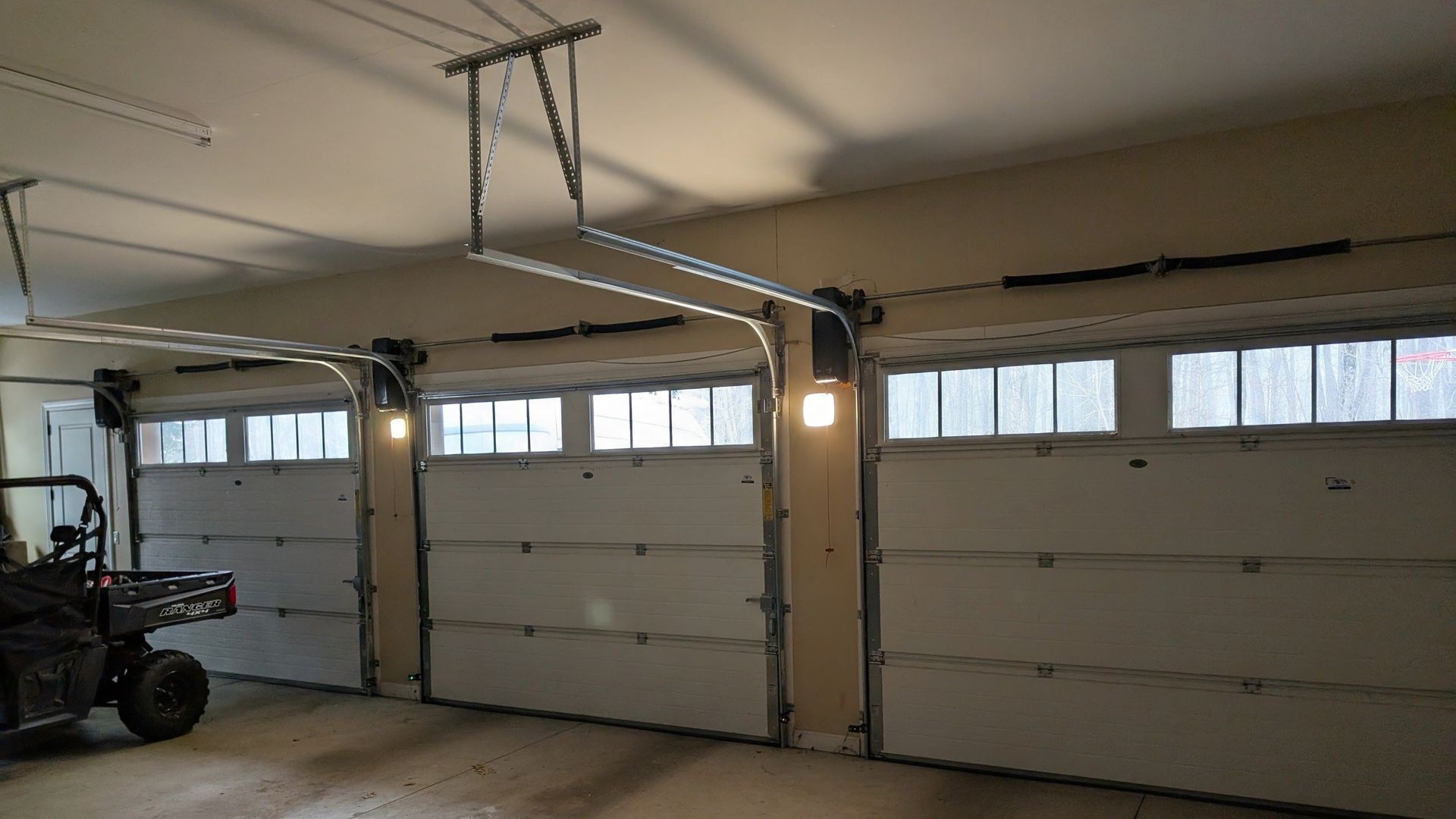 Interior of a garage with three white overhead doors and a parked ATV on the left