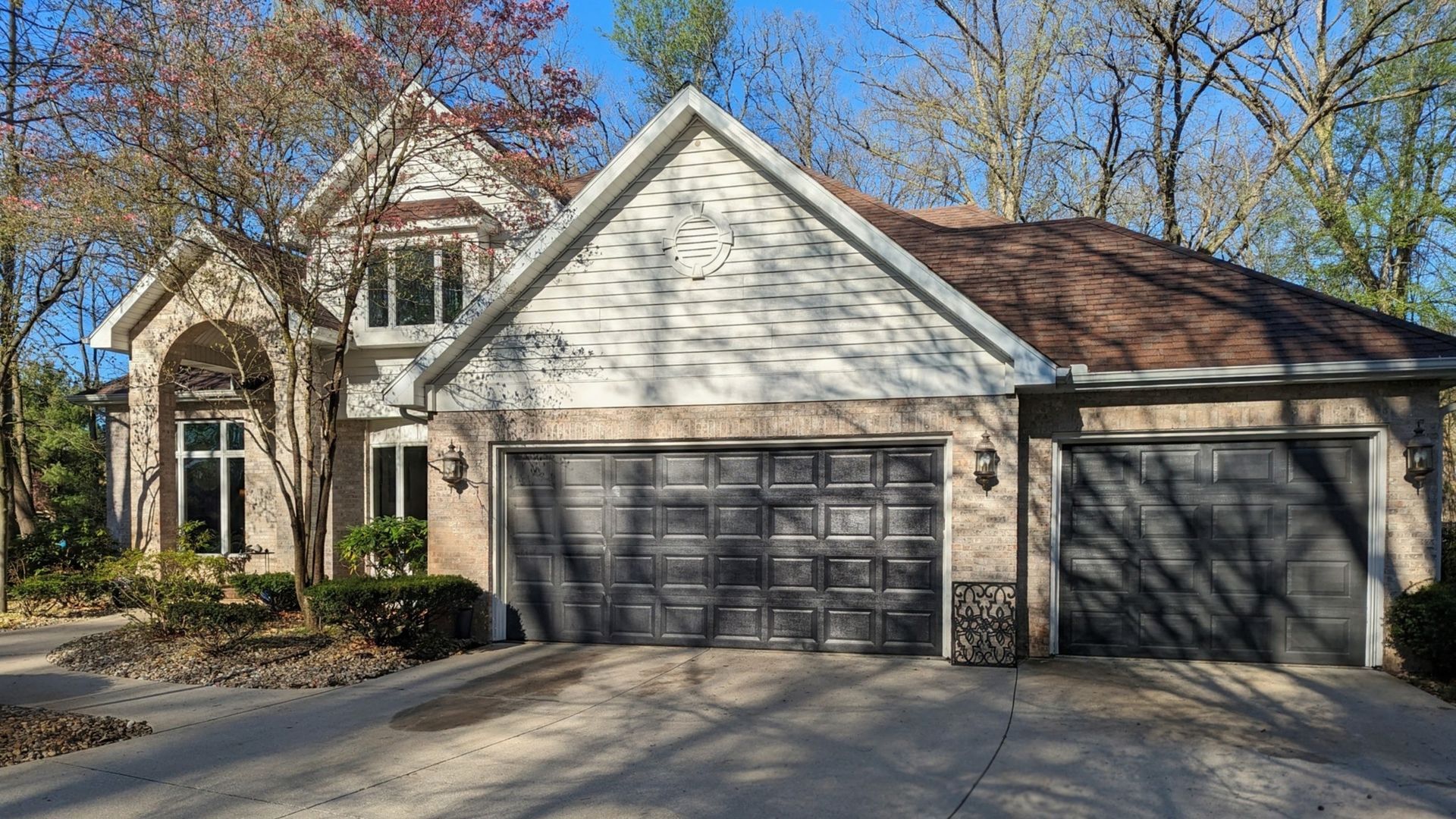 Suburban house with tan siding, stone accents, and a three-car garage under clear blue sky
