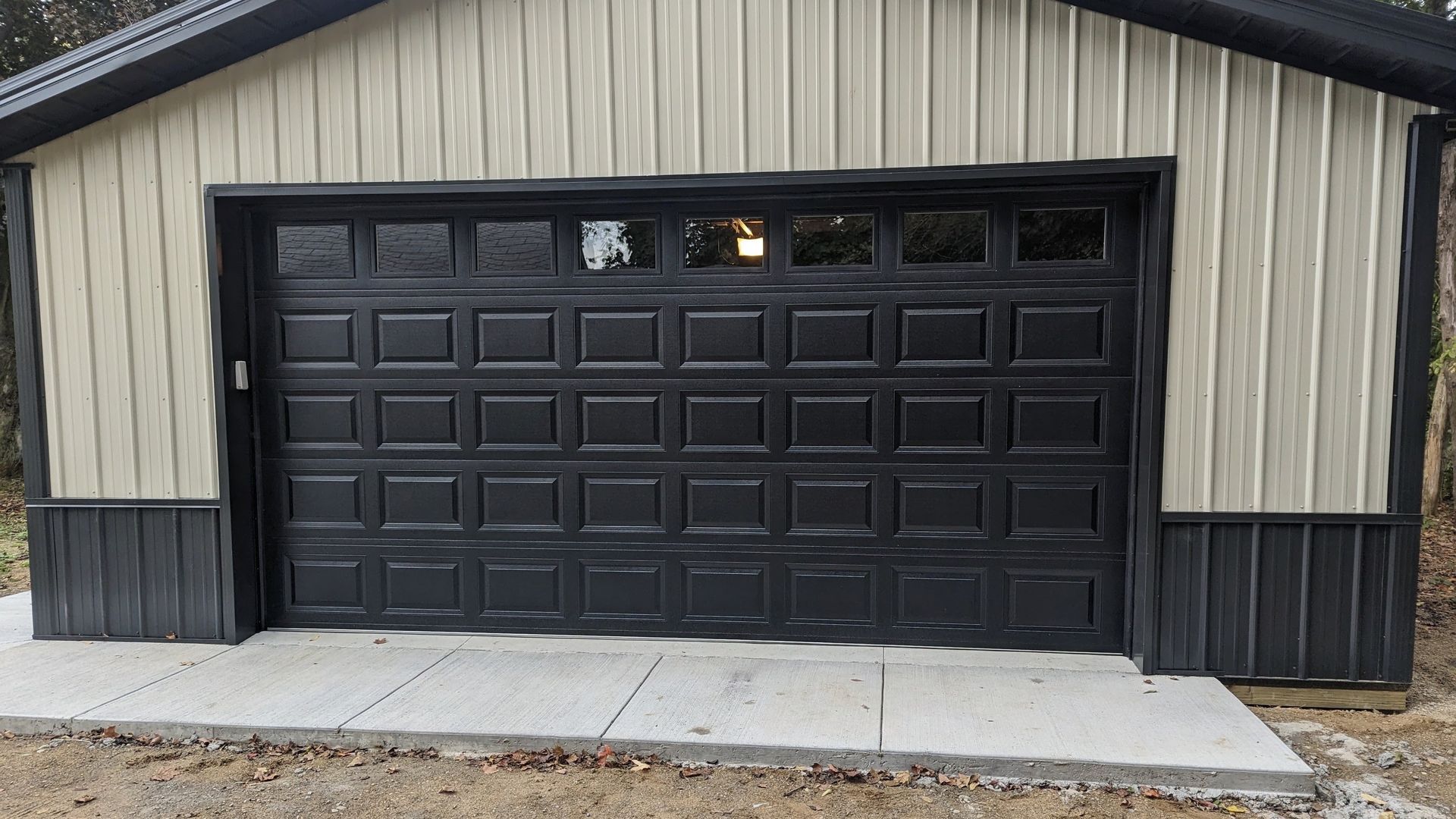 Black garage door on a beige house exterior with a concrete driveway and a small strip of grass.