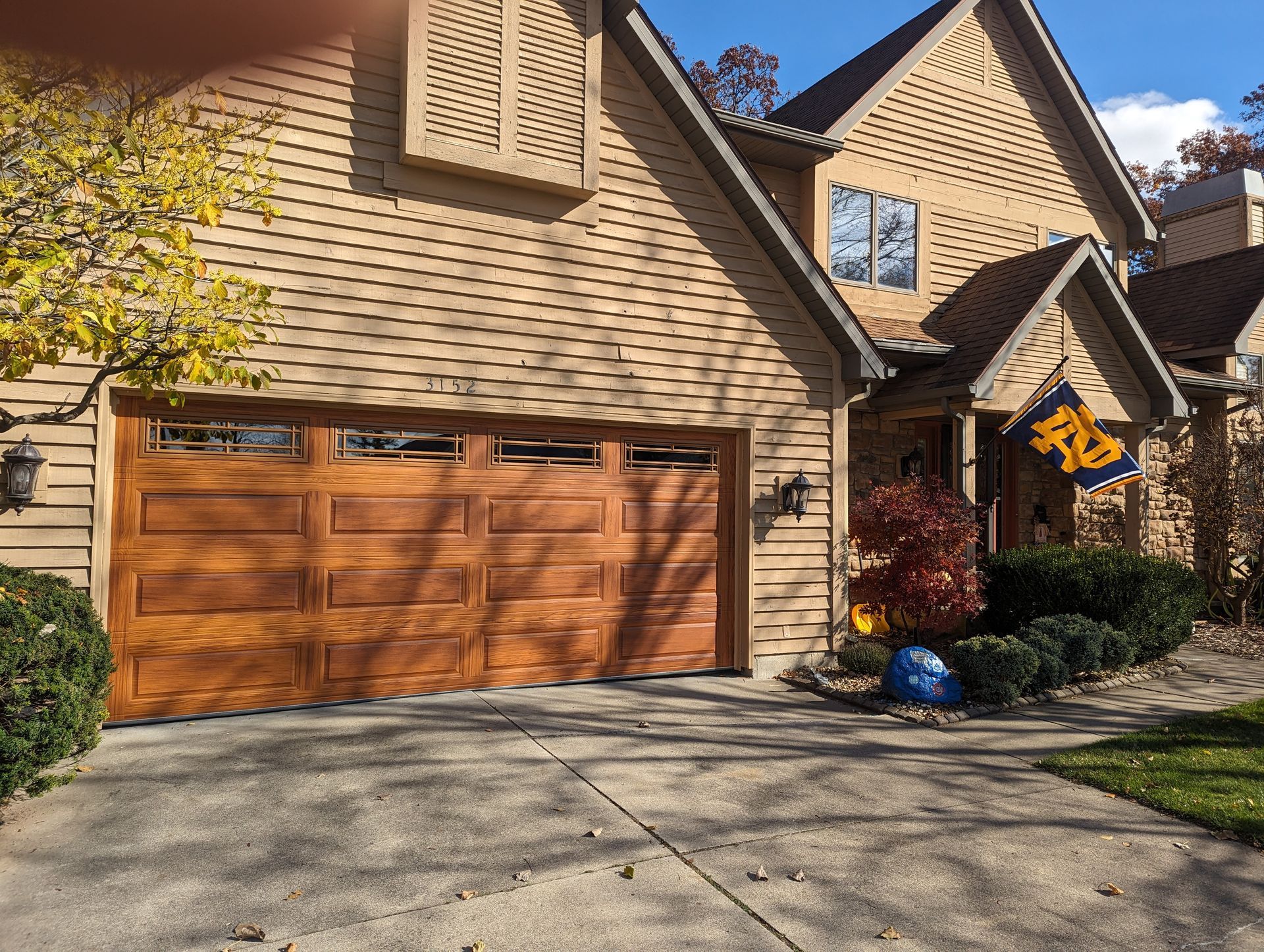 Suburban house with a wooden garage door, stone siding, and a driveway under a sunny sky