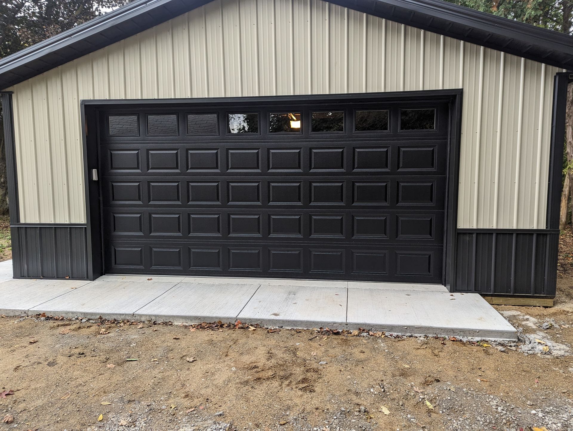 Detached garage with black paneled door and beige siding on a concrete driveway