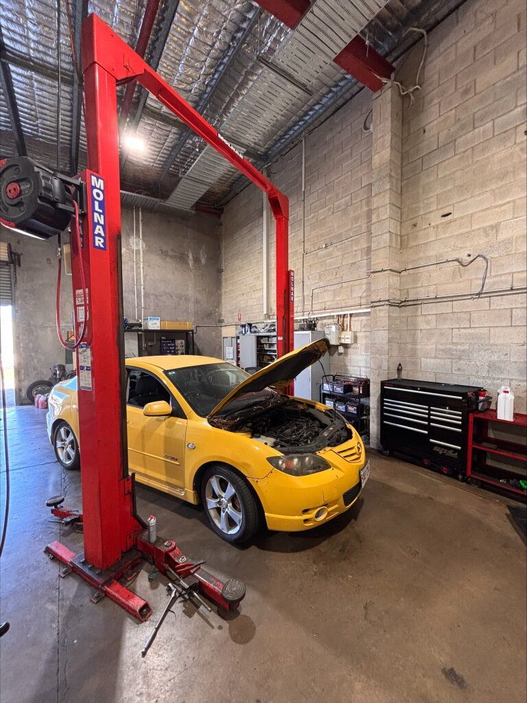 A yellow car is sitting on top of a red lift in a garage. — Kawana Auto Service In Warana, QLD