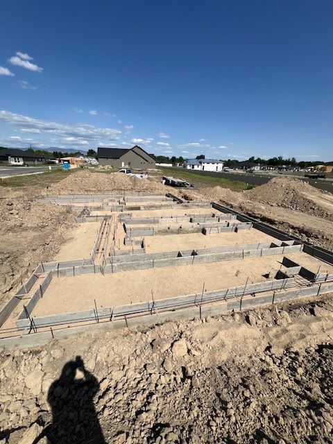 A construction site featuring concrete foundation footings set in a sandy lot under a clear blue sky.