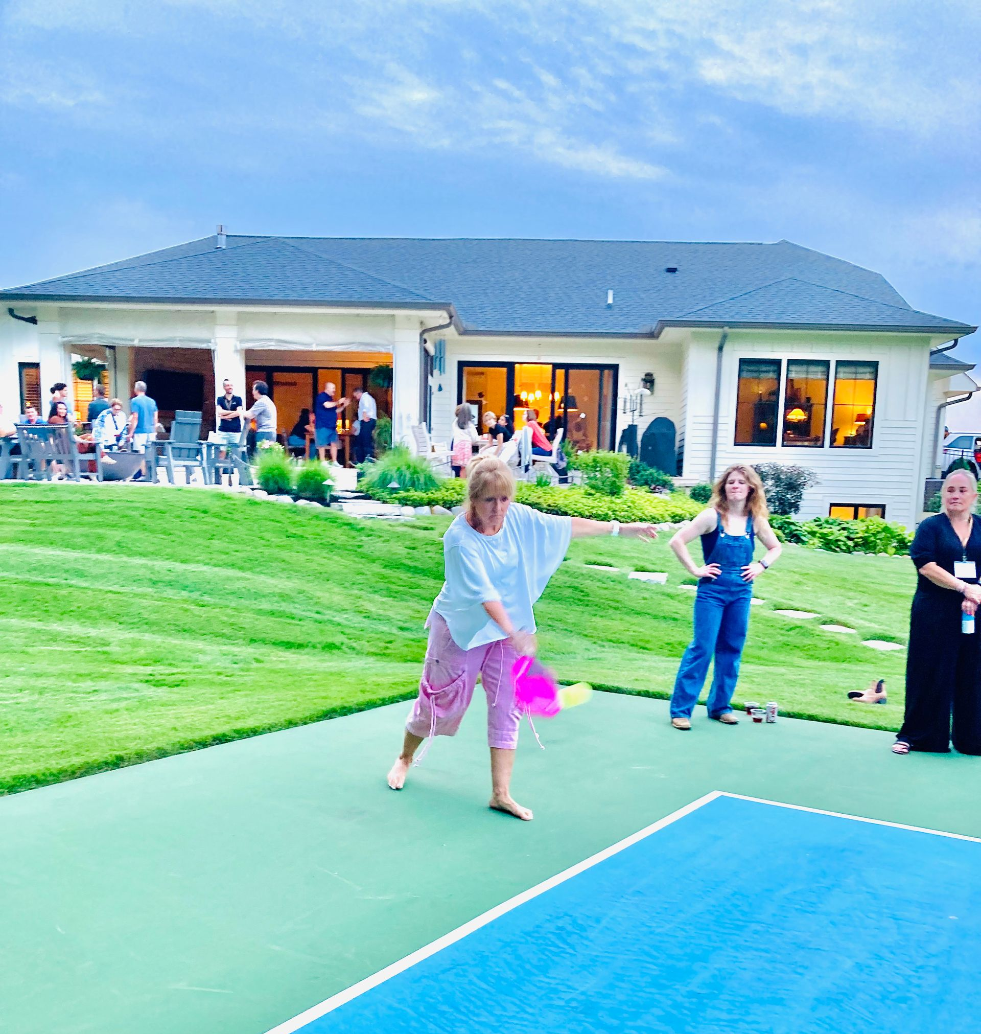 People walking on a green court near a blue sports surface at an outdoor gathering.