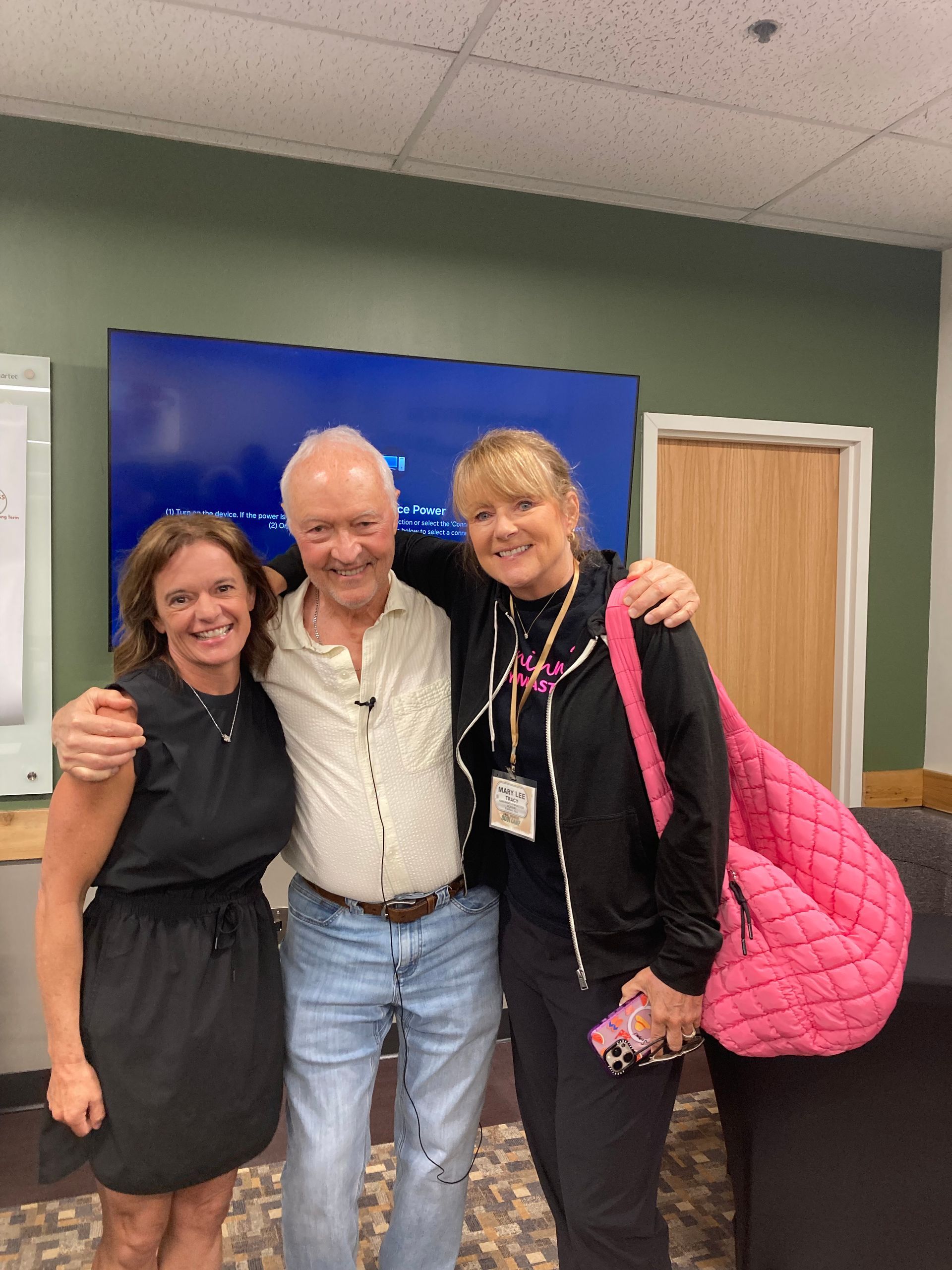 Jen Evans, Jeff Metzger and Mary Lee Tracy smiling and posing indoors, with a blue backdrop and green walls behind them.