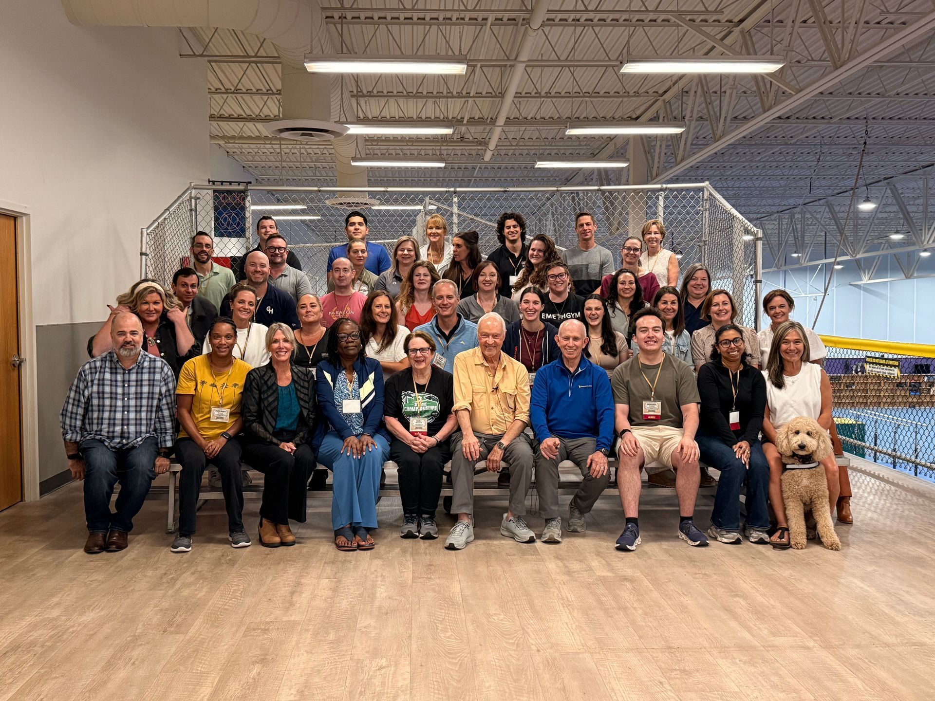 Large group (Boot Camp 76) posing for a photo on steps in a bright indoor space, with a dog at the front right.