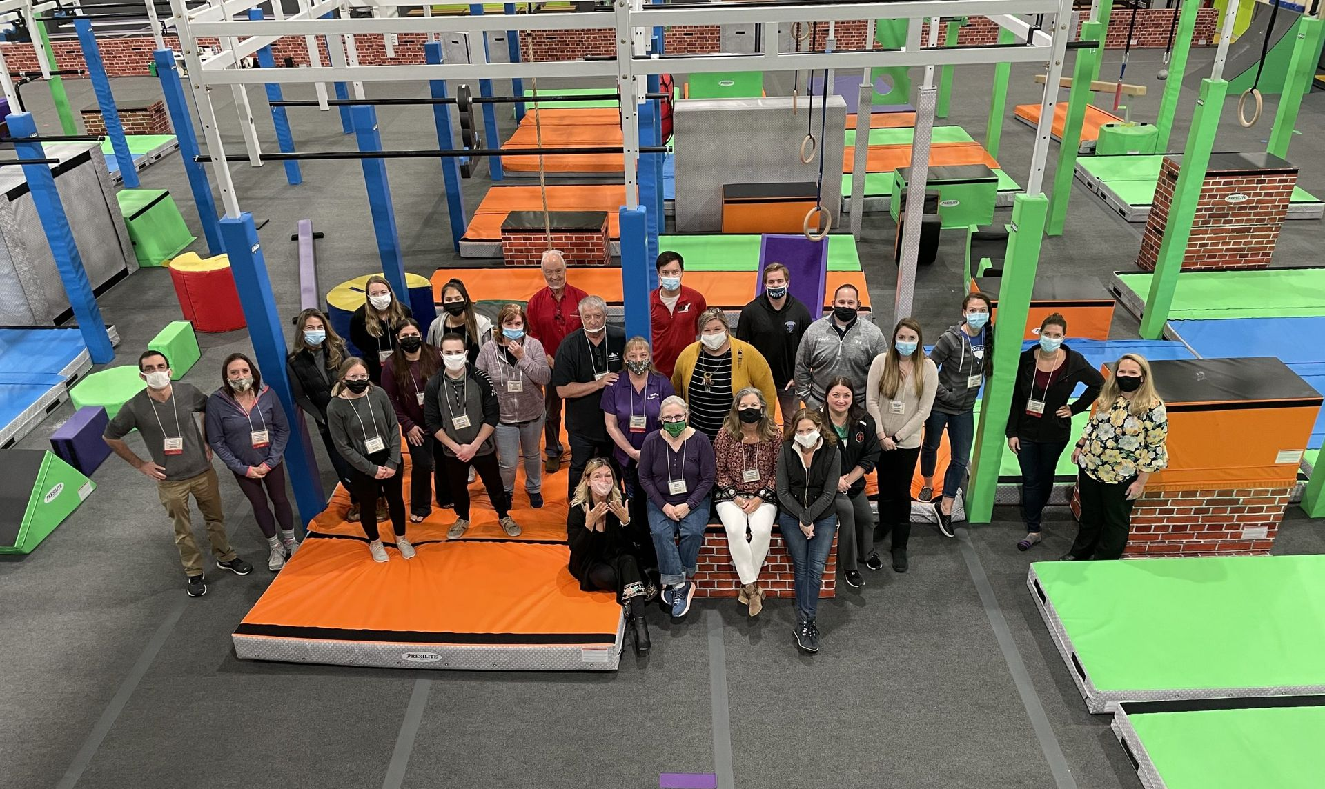 Group of people posing indoors on an orange obstacle platform in a colorful trampoline park