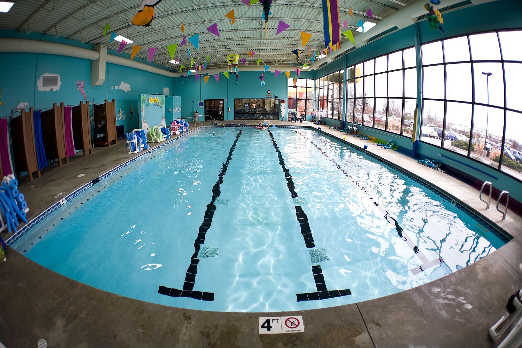 Indoor swimming pool with lap lanes, blue water, and large windows along one side
