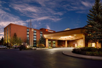 Hotel entrance at dusk with warm lights, brick facade, and a curving driveway under a blue evening sky