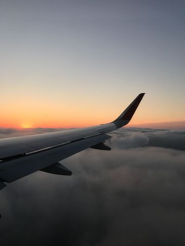 Airplane wing above clouds at sunrise with an orange glow on the horizon
