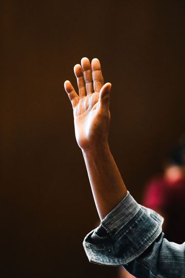 Raised hand with open palm in a long-sleeve shirt against a blurred dark background.