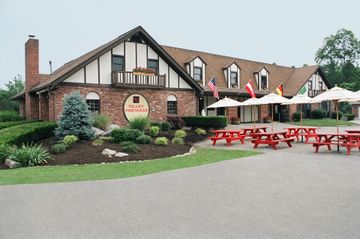Brick restaurant with a balcony, red picnic tables, umbrellas, and a landscaped patio on an overcast day