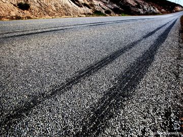 Empty asphalt road with dark tire skid marks curving along a rocky roadside