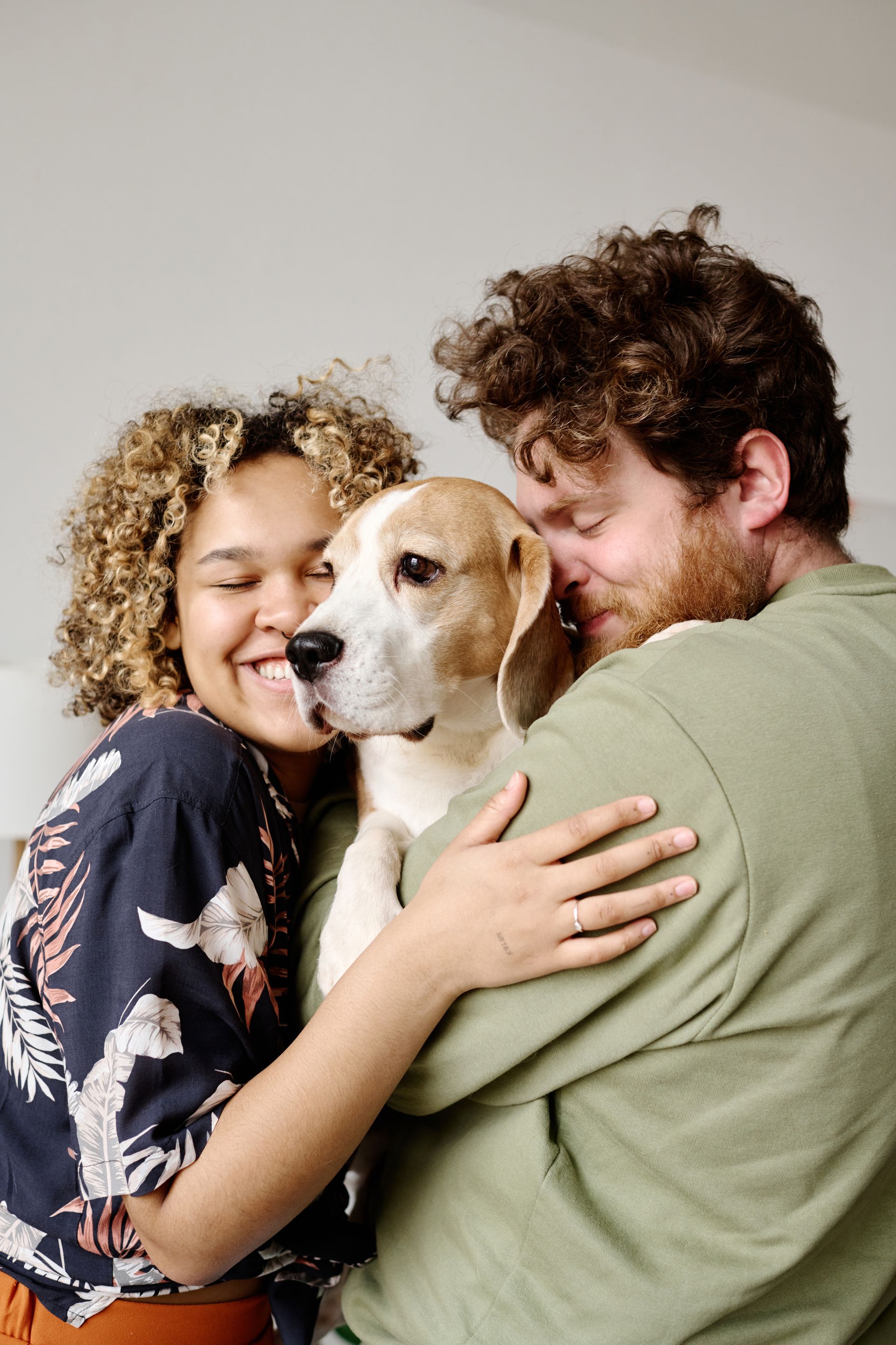 A couple embraces a beagle dog, all smiling indoors.