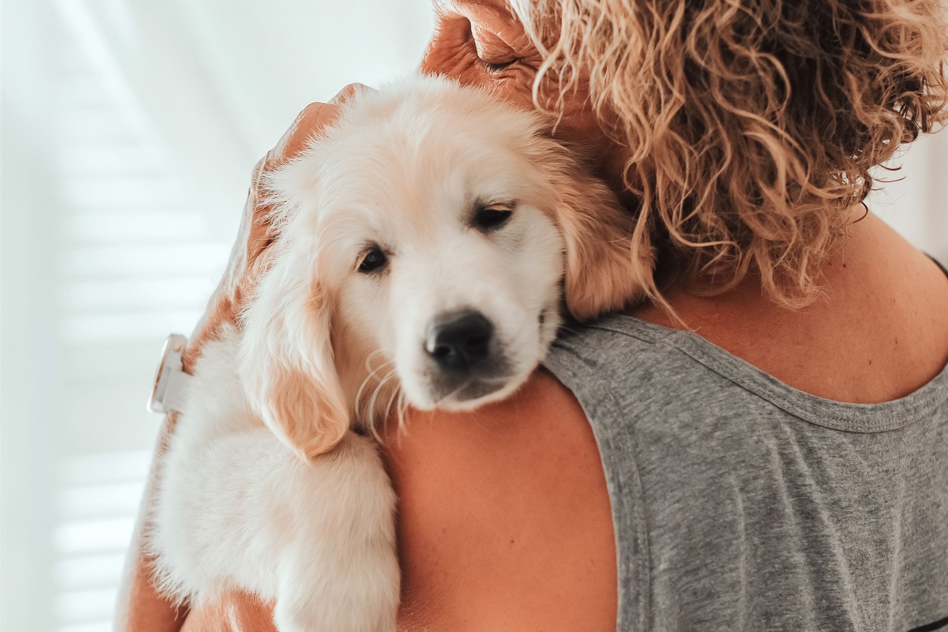 Woman holding a fluffy, light-colored puppy on her shoulder; puppy is resting its head against her.