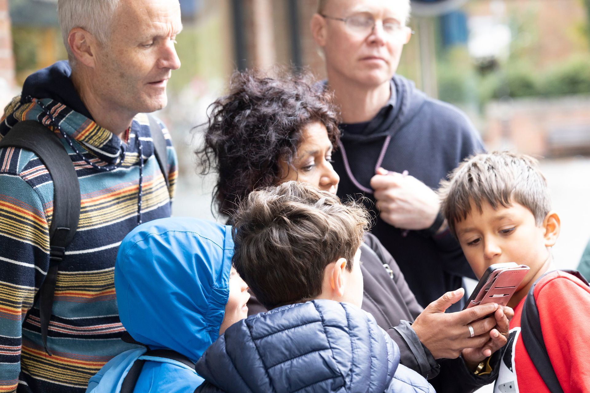 A group of people are standing on a sidewalk looking at their phones.