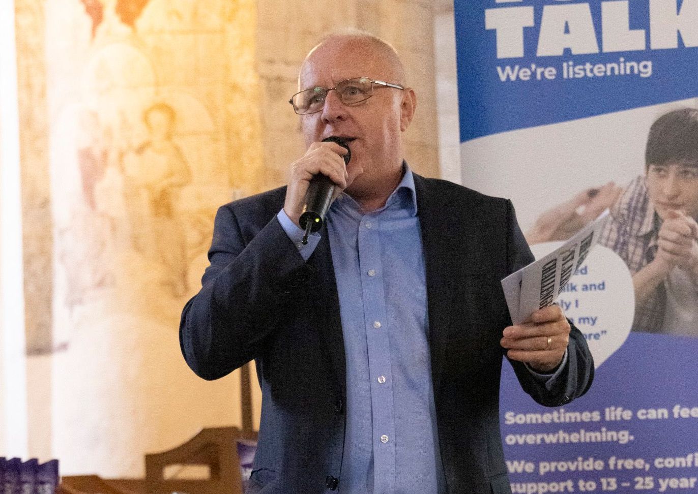 Peter Barker is speaking into a microphone in front of a sign that says Youth Talk