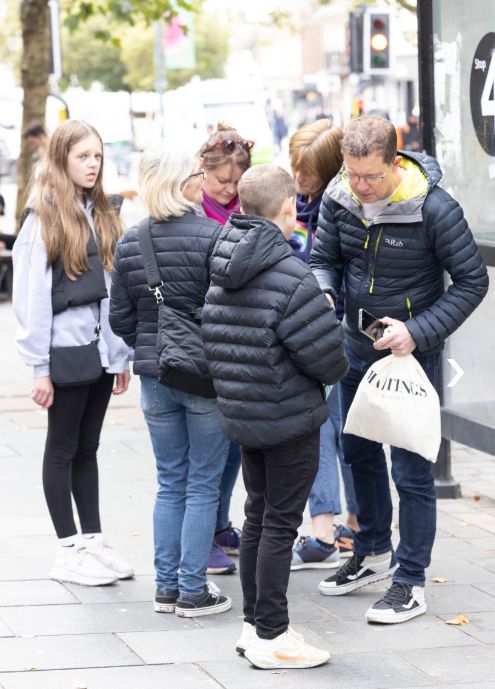 A group of people are standing on a sidewalk talking to each other.