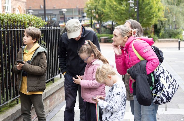 A group of people are standing on a sidewalk looking at their phones.