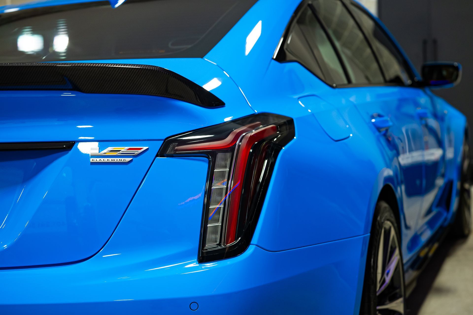 A bright blue Cadillac CT4-V Blackwing sedan, showing the rear taillight and spoiler detail.