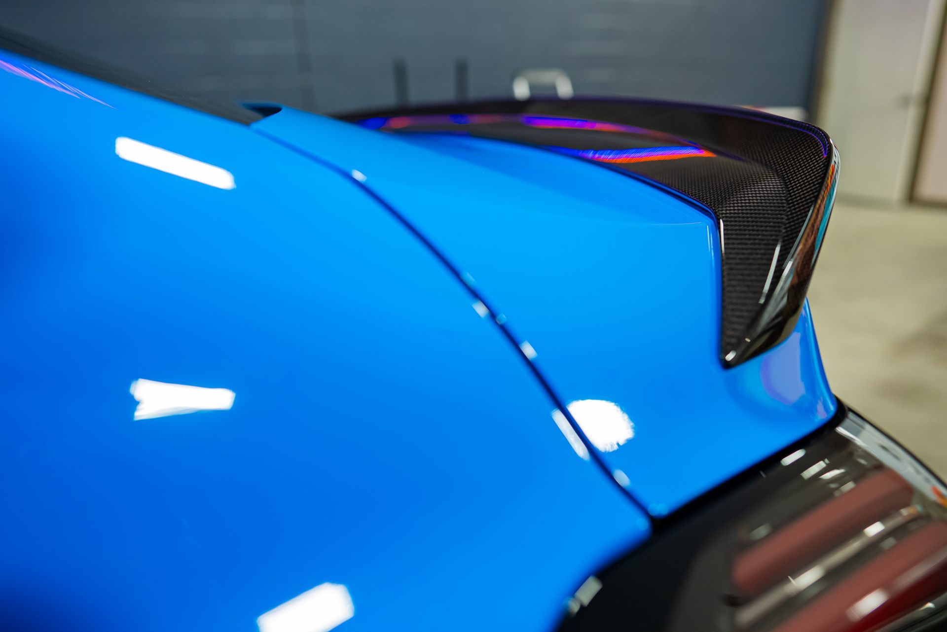 A carbon fiber spoiler on the trunk of a bright blue sports car.