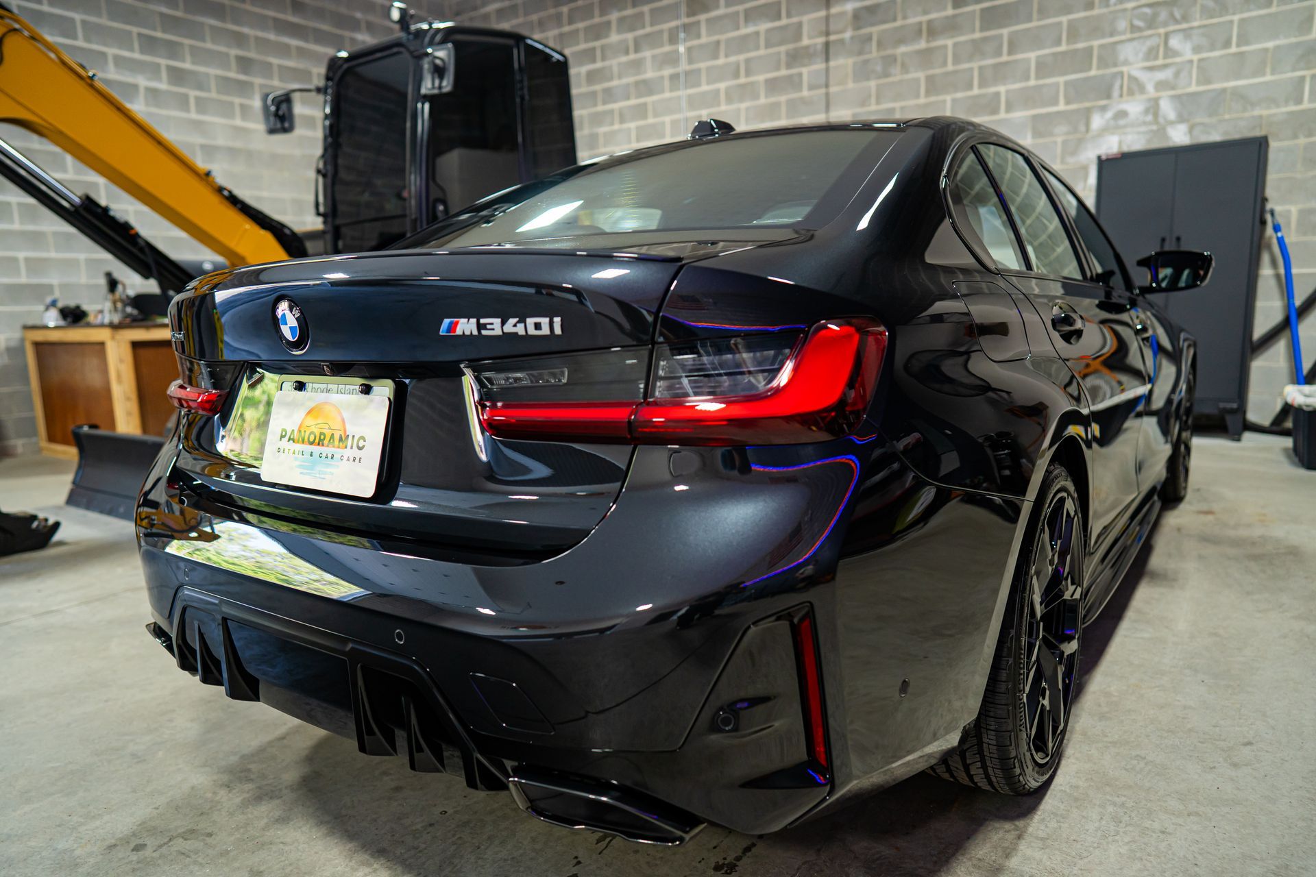 Black BMW sedan in a garage, rear view with a damaged bumper and taillight area.