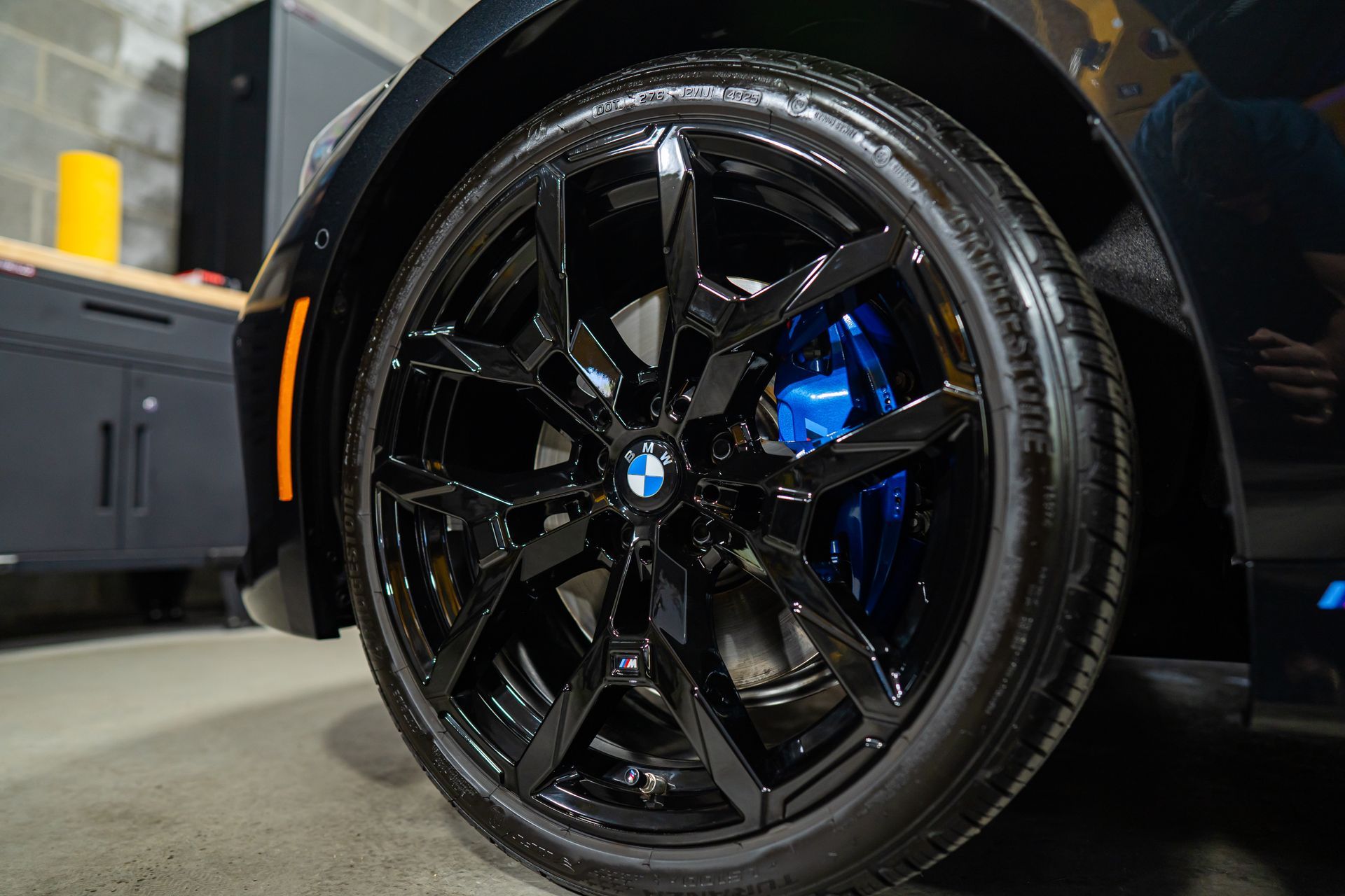 Close-up of a glossy black car wheel with blue brake caliper in a garage