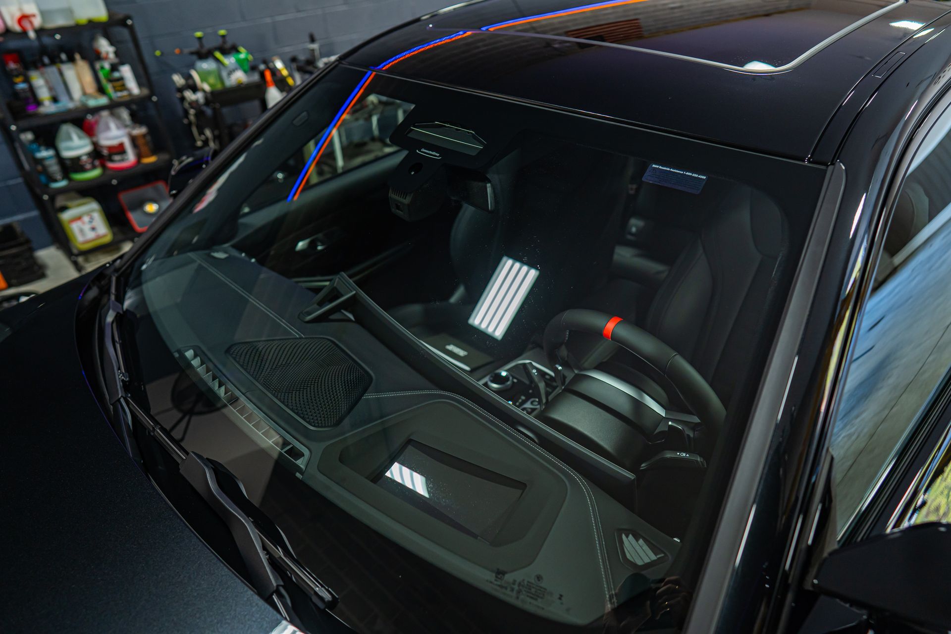 Black car windshield reflecting garage lights, with dashboard and steering wheel visible inside