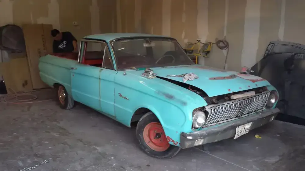 A teal Ford Ranchero parked in a garage with a person working on the interior.