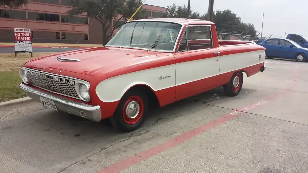 A two-tone red and white vintage Ford Falcon Ranchero parked in a paved outdoor lot.