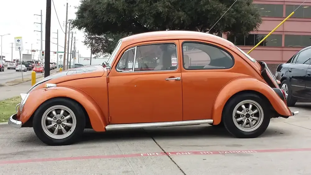 A bright orange vintage Volkswagen Beetle parked on a concrete lot near a street.