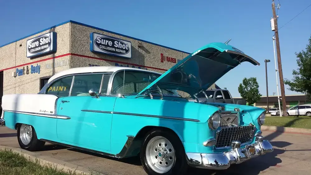 Turquoise-and-white vintage car with hood open parked outside a tire shop