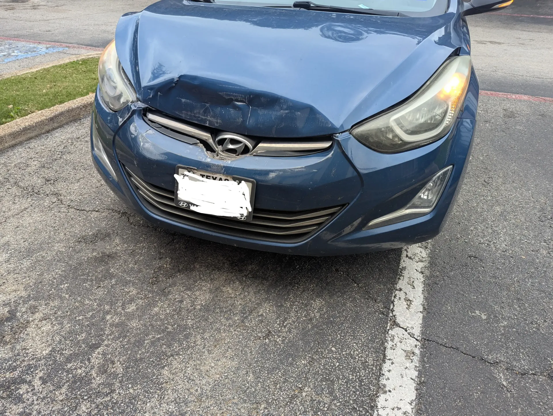 A dark blue Hyundai sedan parked on asphalt, showing significant front-end collision damage to the hood and grille.