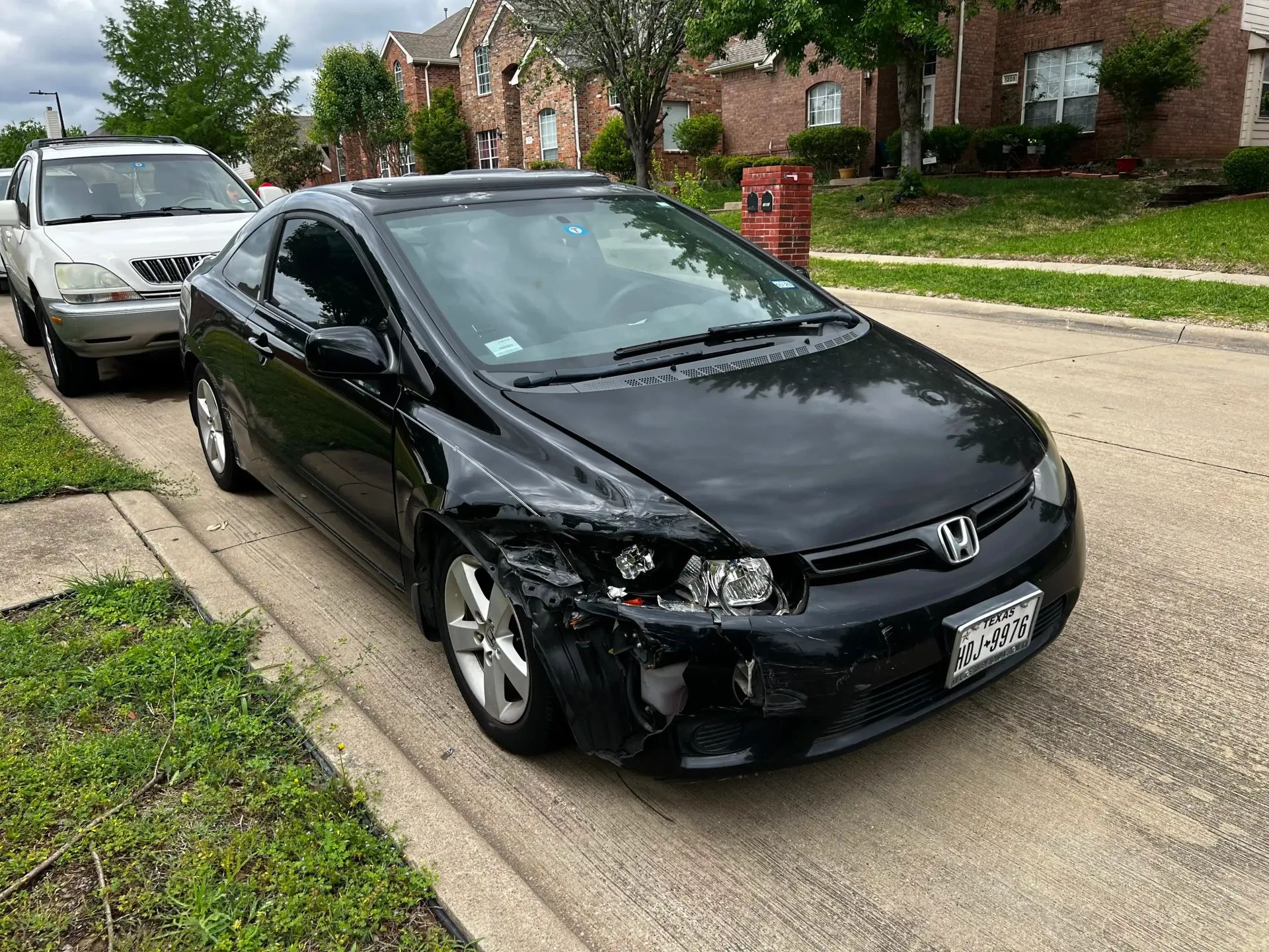 Black Honda coupe parked on a residential street with significant front-passenger-side bumper and fender damage.
