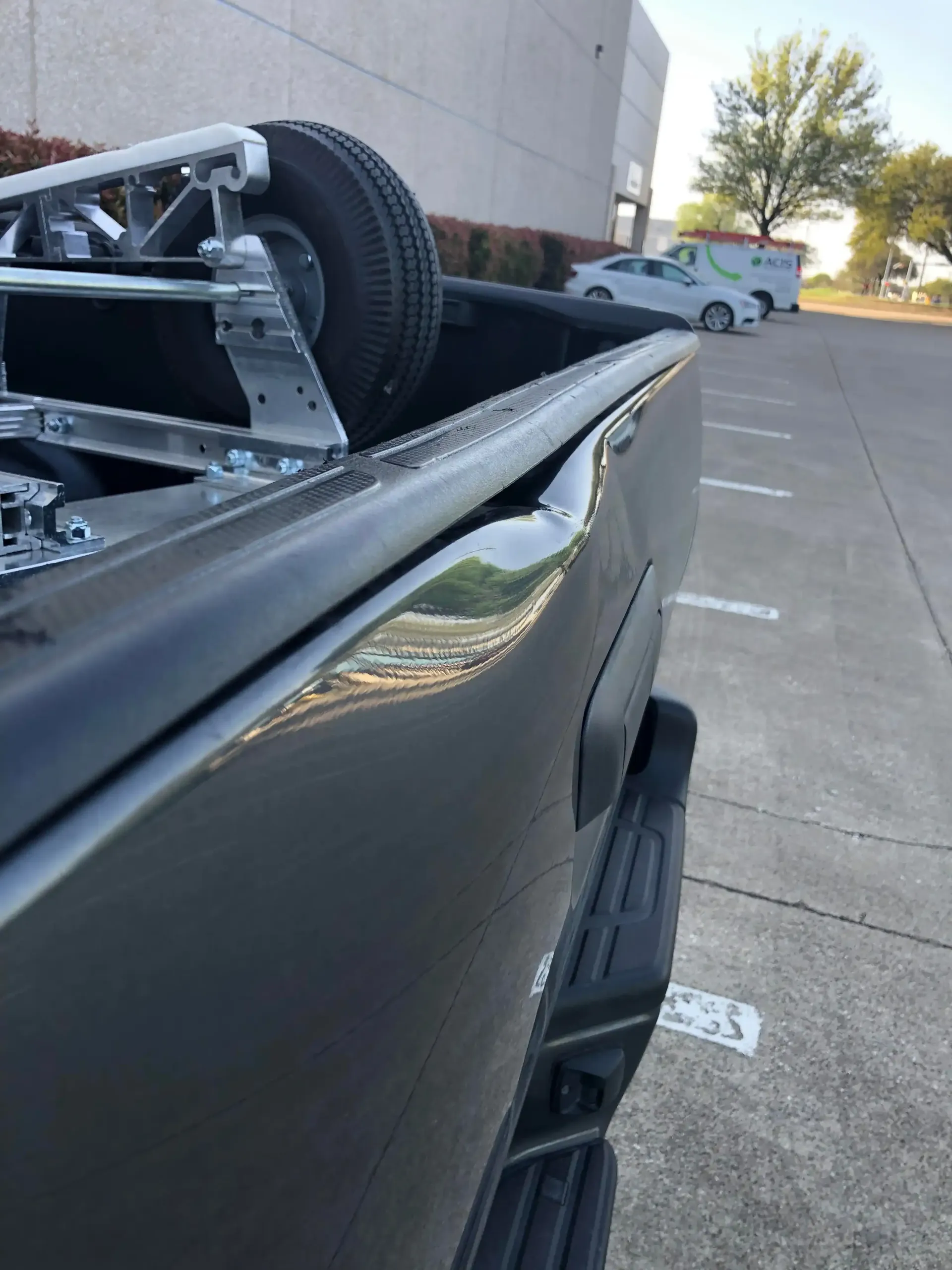 A close-up view of a deep dent along the top edge of a dark pickup truck bed, with a cart wheel visible inside.
