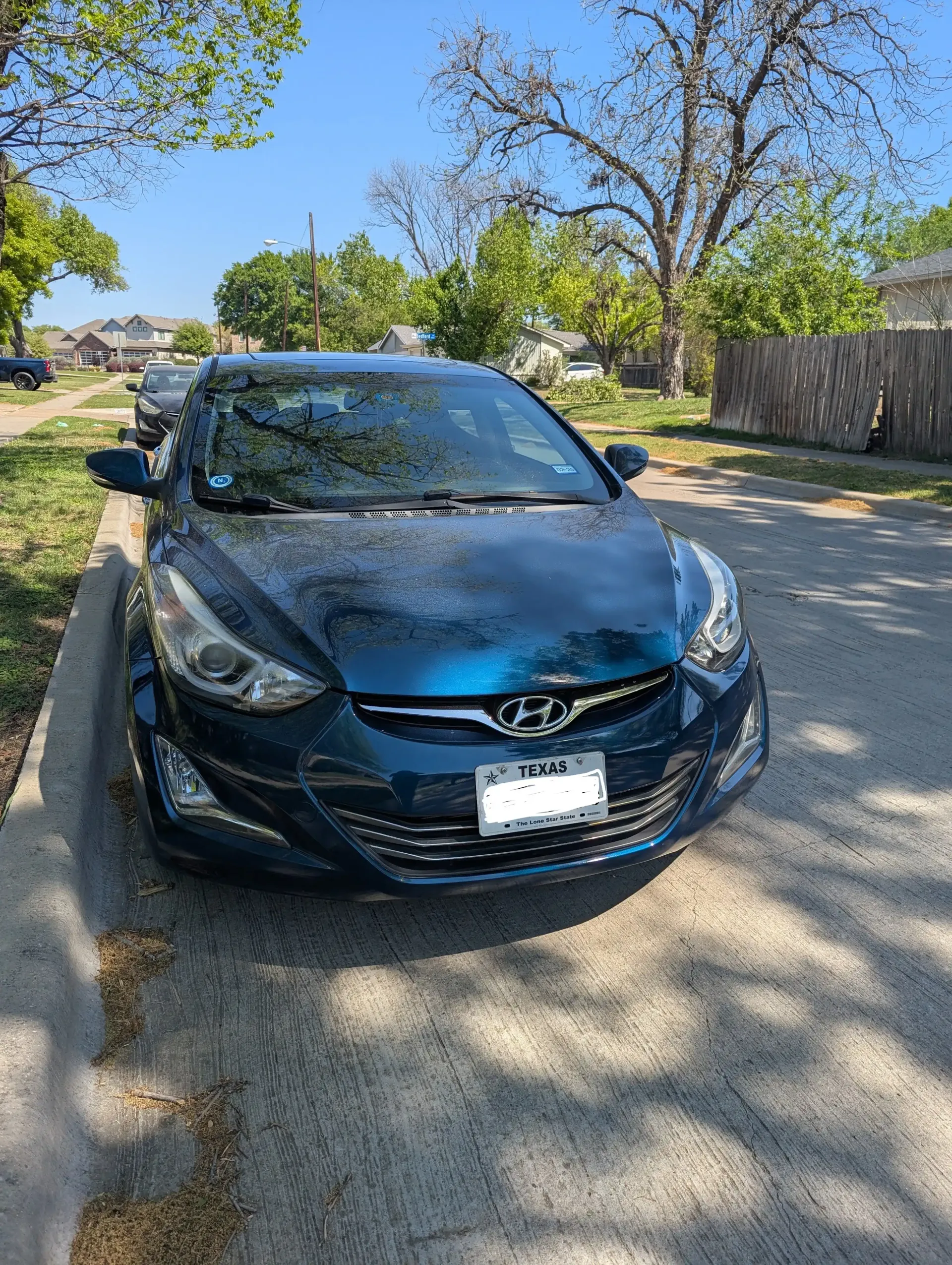 A teal Hyundai Elantra parked on a residential street on a sunny day.