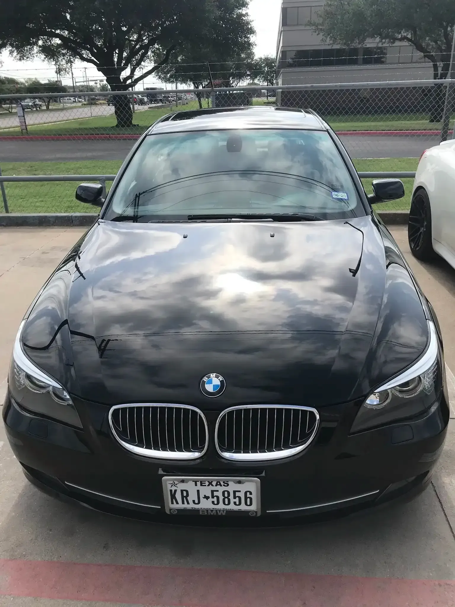A black BMW sedan parked in an outdoor lot with a Texas license plate visible on the front bumper.