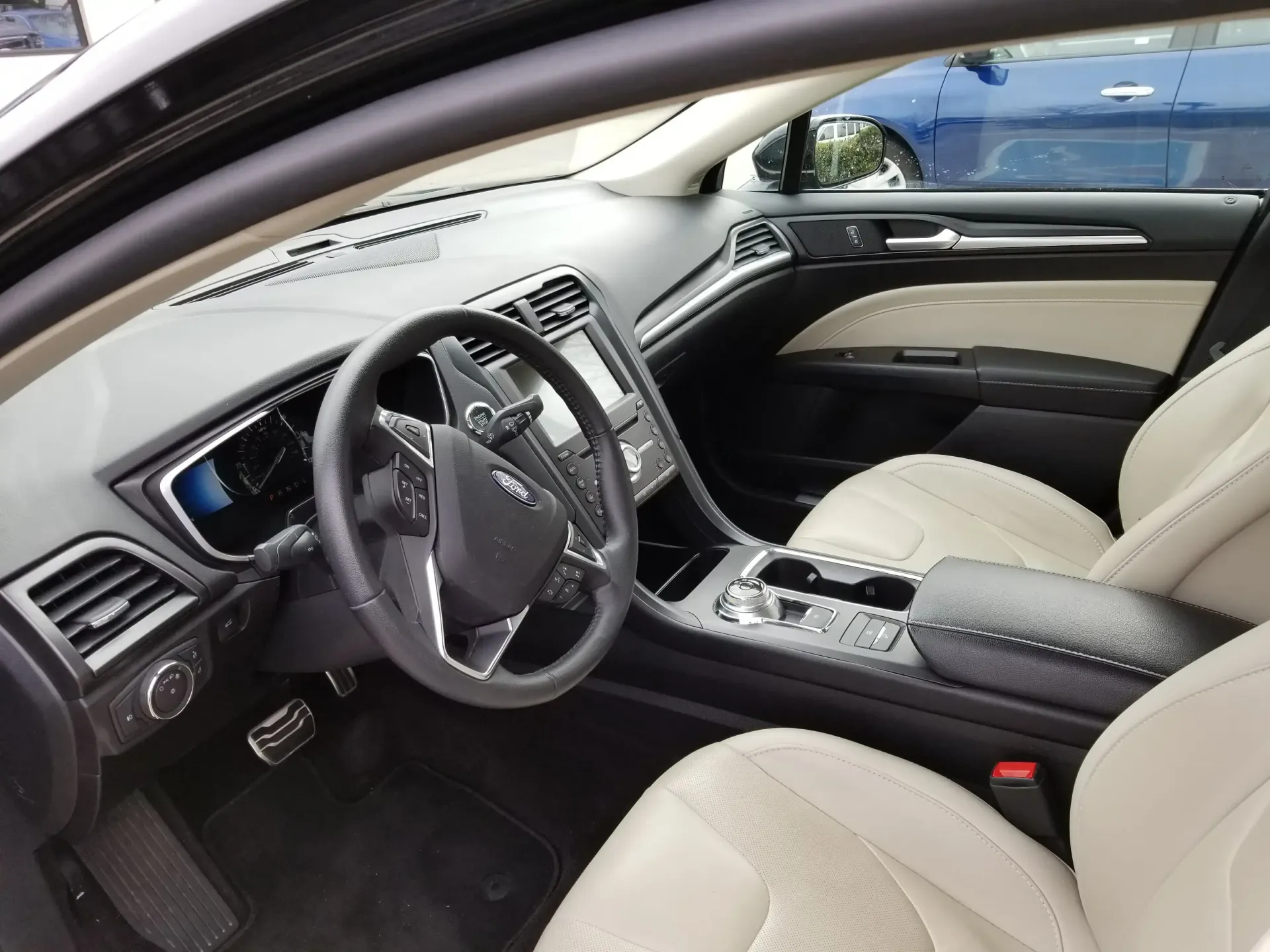 Interior view of a car cockpit featuring a black steering wheel, dashboard, and cream-colored leather seats.