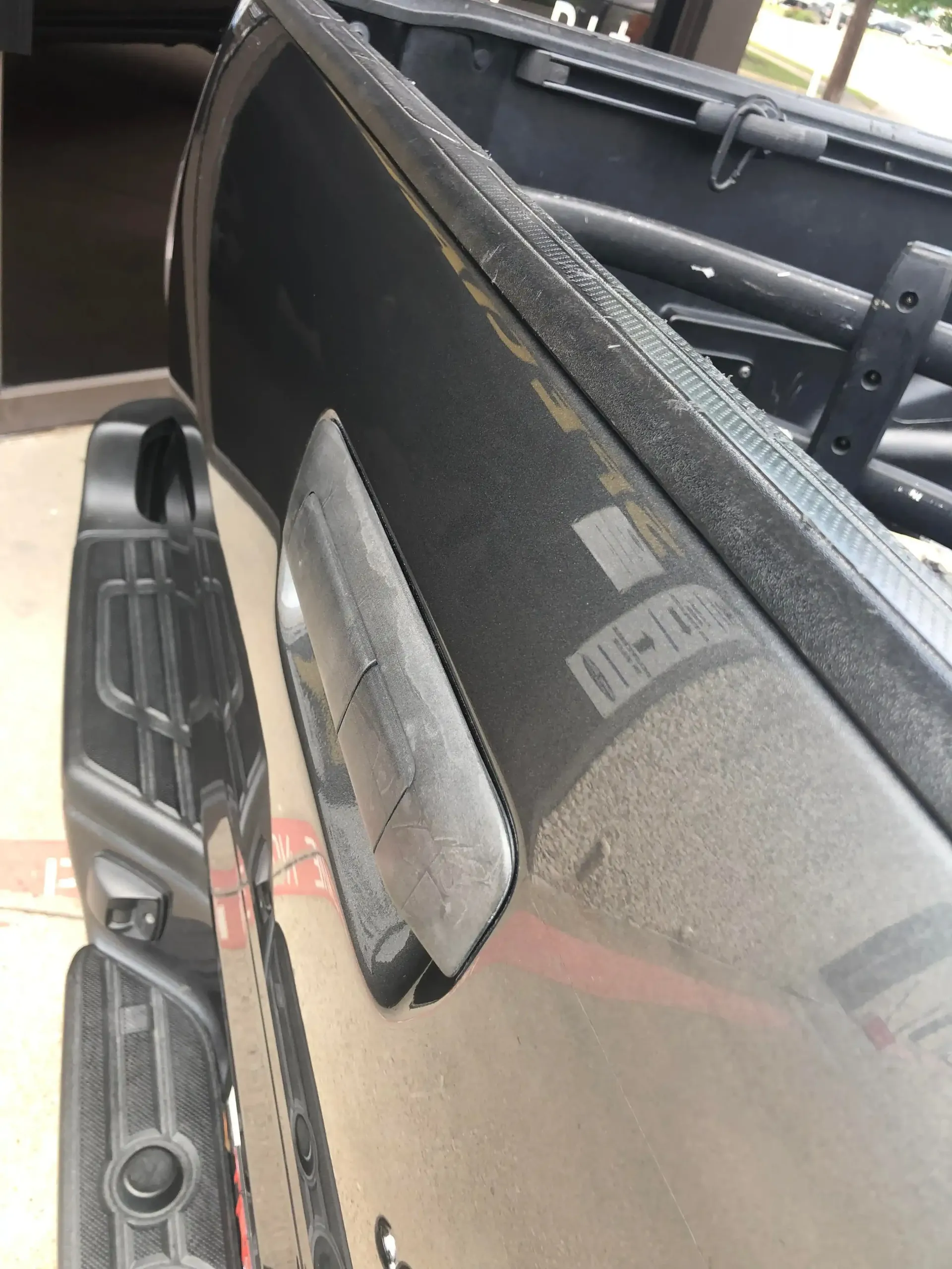 Close-up of a black truck's tailgate and rear bumper, showing the handle assembly and textured trim.