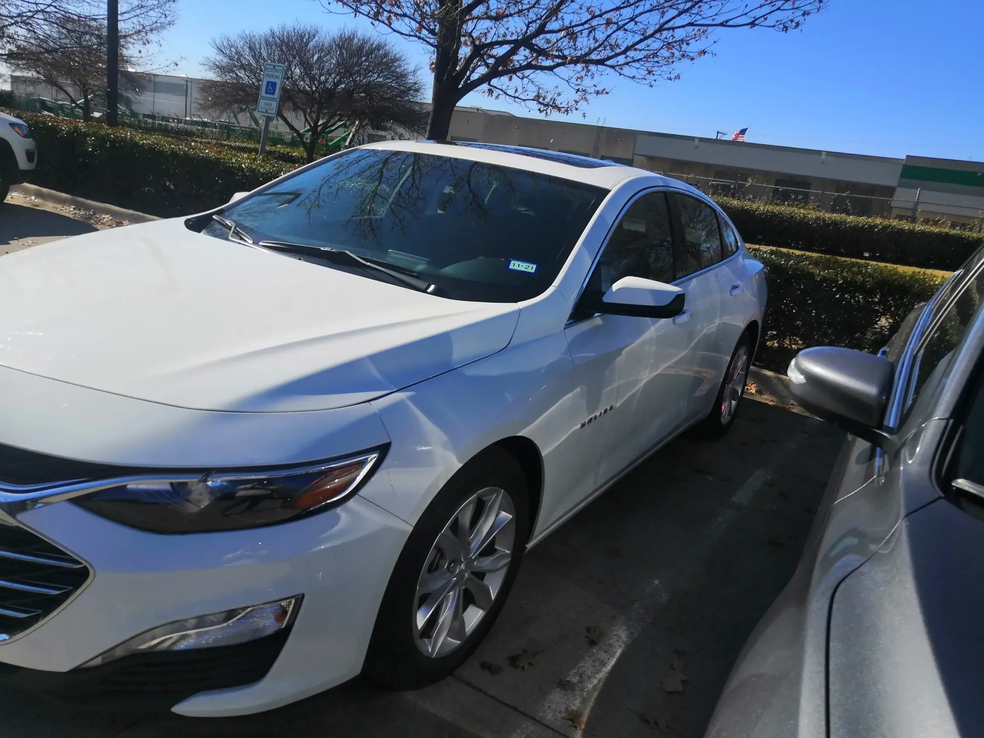 A white Chevrolet Malibu parked in an outdoor lot on a sunny day next to a gray car.