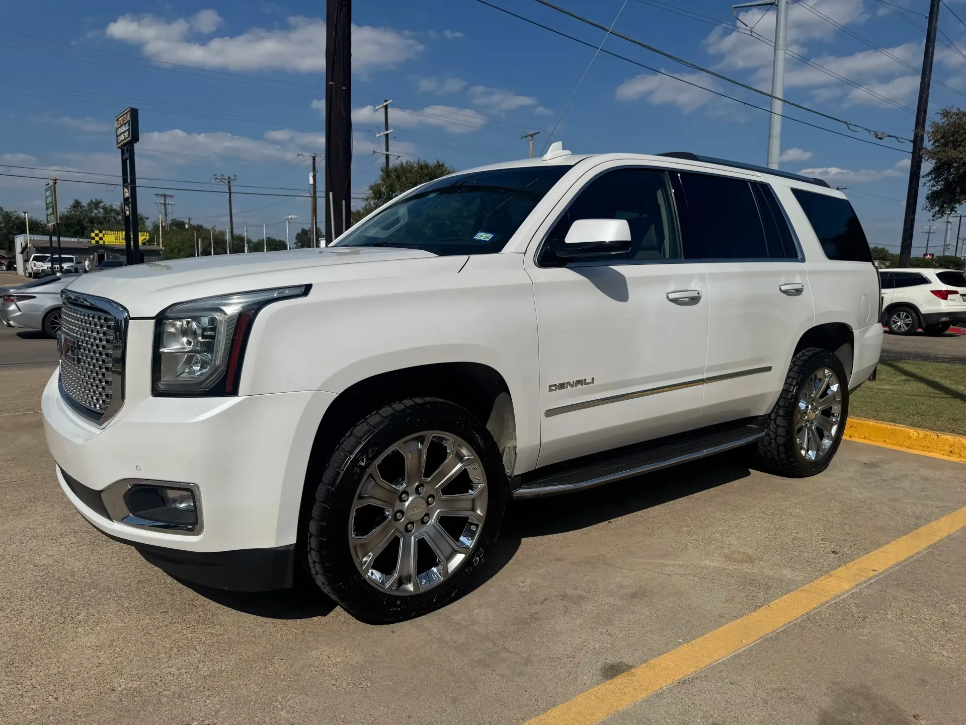 A white GMC Yukon SUV parked on a paved lot on a sunny day.