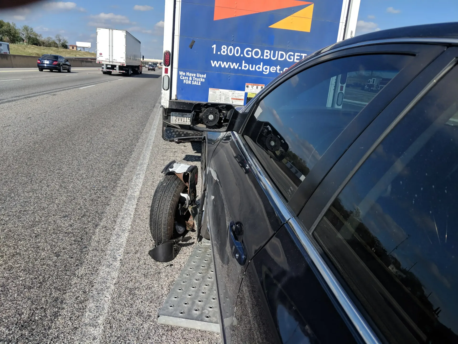 Damaged car and motorcycle stopped on highway shoulder beside a blue truck