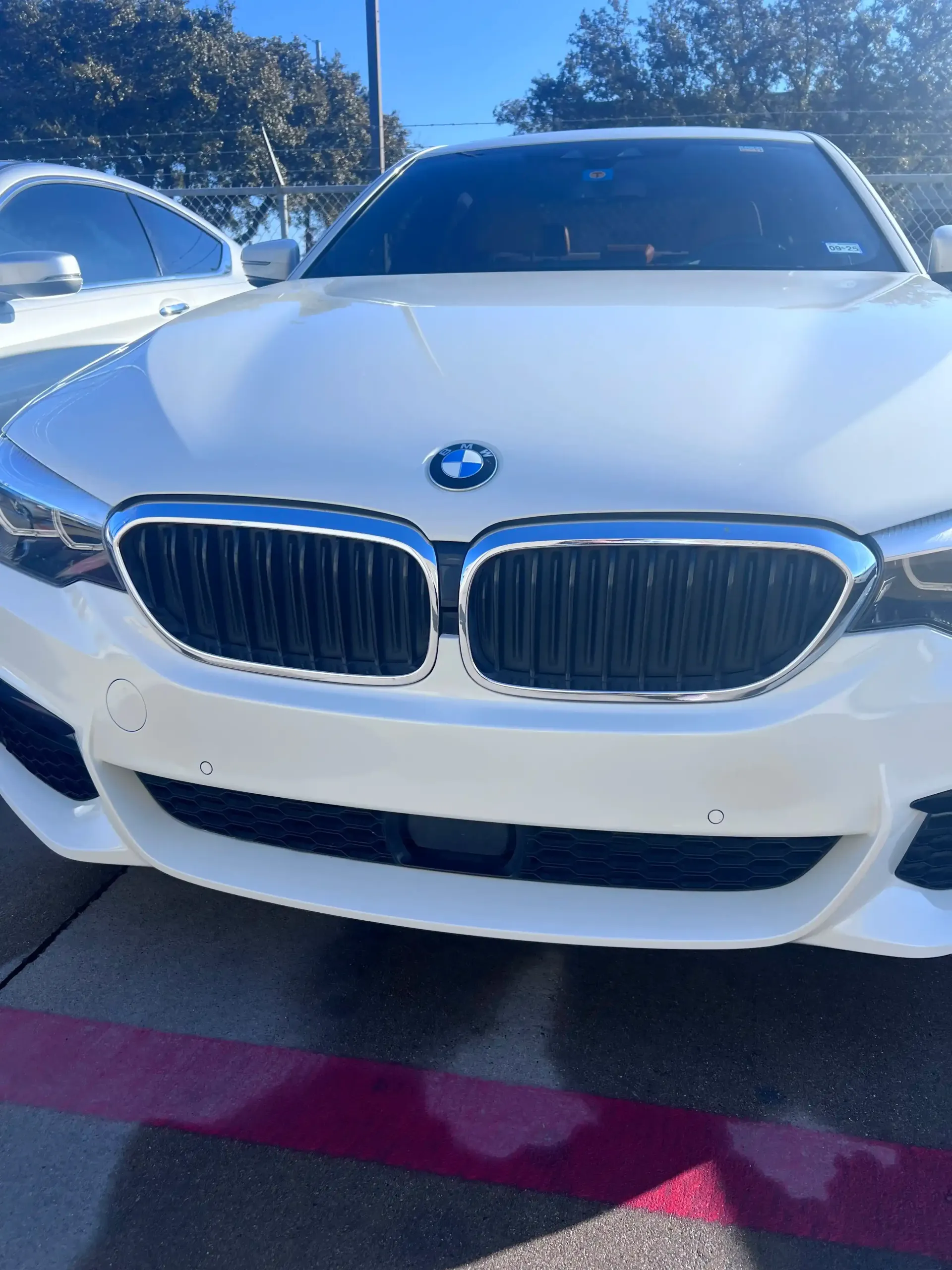A close-up, front-facing view of a white BMW sedan parked on a sunny day.
