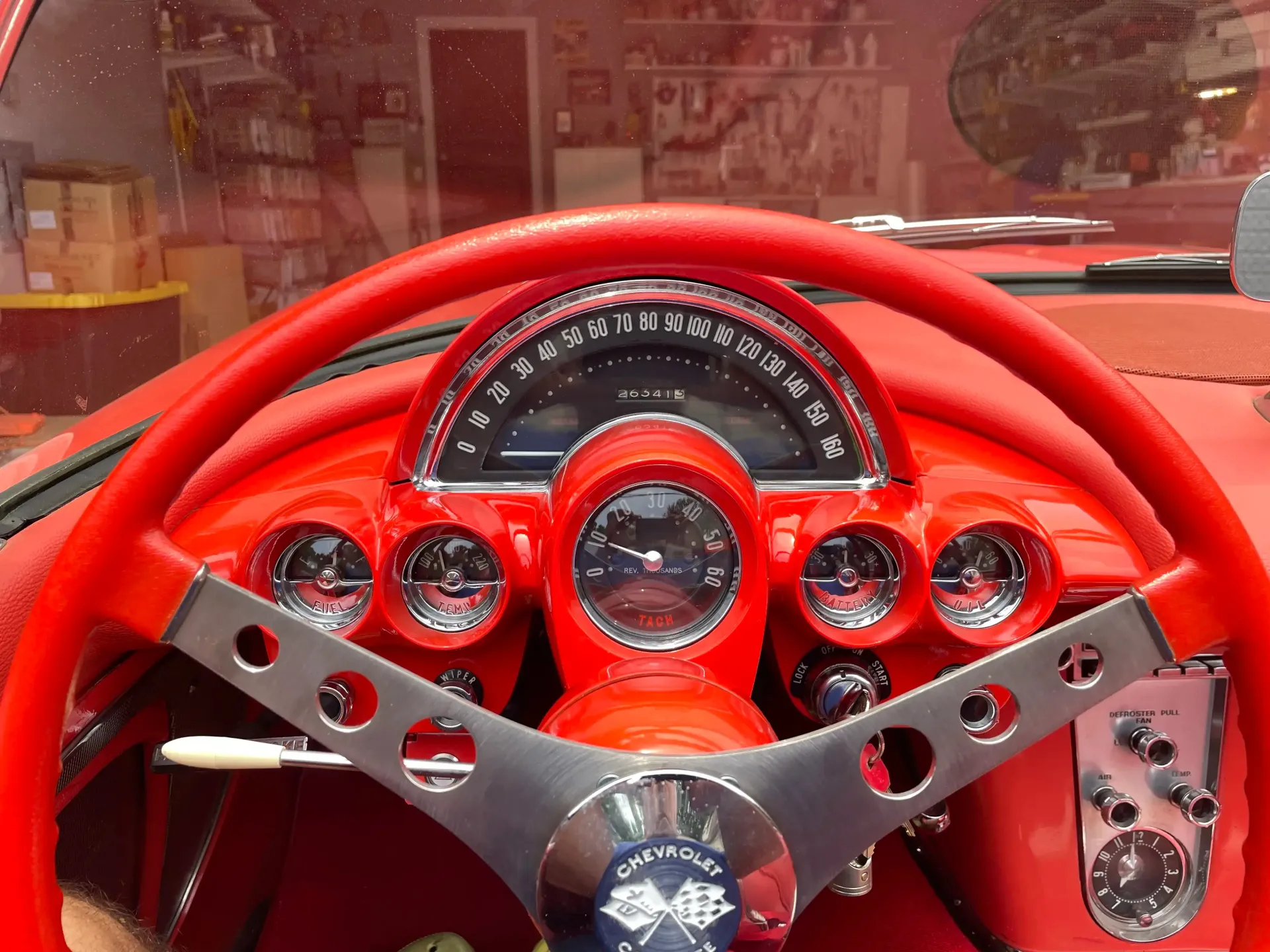 Interior of a classic red Chevrolet Corvette, focusing on the steering wheel, chrome-rimmed dashboard gauges, and clock.